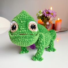 a green crocheted frog toy with eyes and legs, sitting on a table