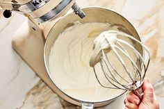 a hand holding a whisk in a metal bowl on top of a counter