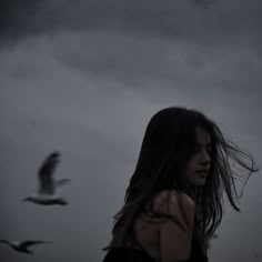 a woman with long hair standing in front of a bird flying over her head and looking into the distance