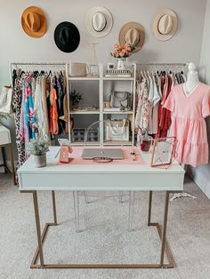 a white table topped with lots of hats and clothing next to a shelf filled with clothes