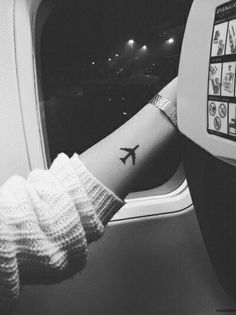 a person's arm with a small airplane tattoo on it, sitting in an airplane