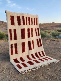 a red and white blanket sitting on top of a dirt field