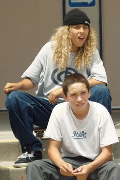 two people sitting on steps with one holding a skateboard and the other looking surprised