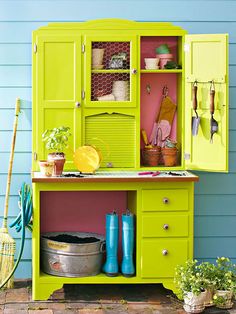 a green cabinet sitting on top of a wooden floor next to a blue wall and potted plants