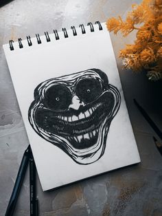 a drawing of a clown's face on a notebook next to some pencils