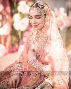 a woman in a pink and gold bridal outfit sitting on the ground with flowers behind her