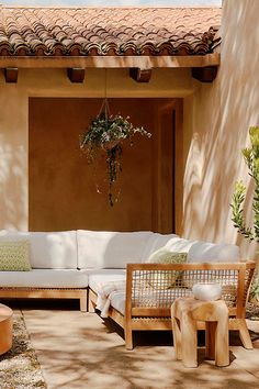 an outdoor living area with white couches and wooden chairs, potted plants on the patio