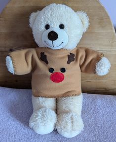 a white teddy bear wearing a brown sweater and red nose sitting on a wooden chair