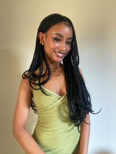 a woman with long braids standing in front of a wall wearing a green dress