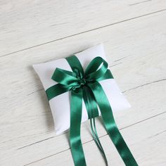 a white pillow with a green ribbon tied around it on top of a wooden floor