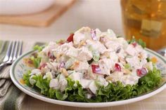 a white plate topped with a salad next to a fork and glass filled with liquid