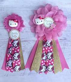 two pink and gold ribbon flowers with hello kitty on the top one is holding a hello kitty brooch