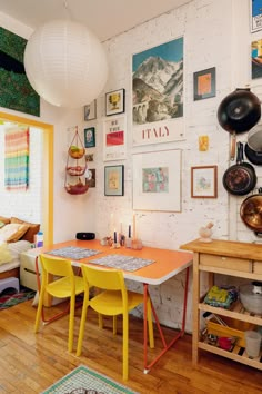 a dining room table with yellow chairs and pictures on the wall