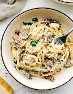 a bowl filled with pasta and spinach on top of a white tablecloth next to a fork