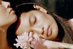 two beautiful women laying down next to each other with flowers in their hair and one has her eyes closed