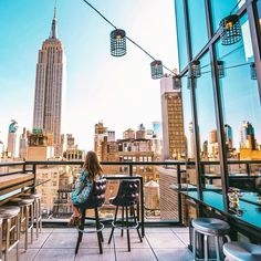 a woman sitting at a table on top of a building looking out over the city