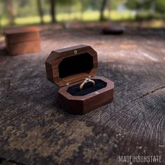 an open wooden box with a wedding ring inside on top of a piece of wood