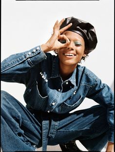 a woman in jeans and a black hat is sitting on the ground with her hands behind her head