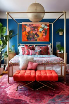 a bedroom with blue walls, pink and orange bedding, red ottomans and an art work on the wall