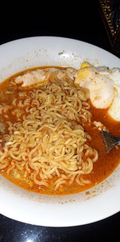 a white plate topped with noodles and meat on top of a black table next to an egg