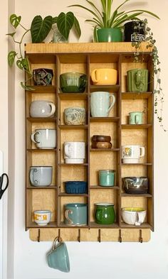 a wooden shelf filled with lots of different types of cups and saucers next to a potted plant