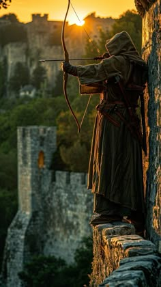 a man with a bow and arrow standing on the side of a building at sunset