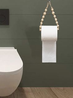 a roll of toilet paper hanging from a rope next to a white toilet in a bathroom