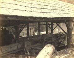 an old black and white photo of men working in a wood shed with logs on the ground