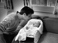 a man kissing the nose of a baby who is in a bassinet on a couch