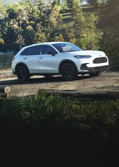 a white suv parked on the side of a dirt road next to trees and water