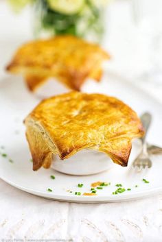 two pieces of food on a white plate with spoons and flowers in the background