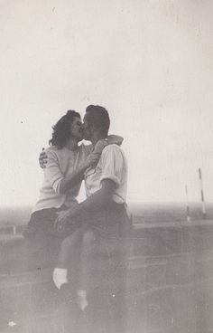 an old photo of two people sitting on a bench kissing each other with the sky in the background