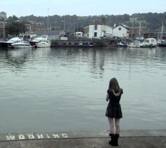 a girl standing on the edge of a dock looking at boats docked in the water