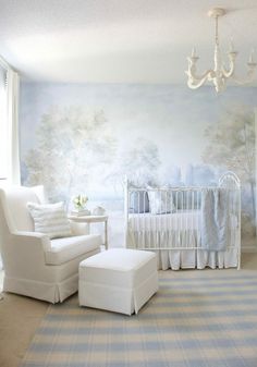 a baby's room with a white crib, chair and wall mural in the background