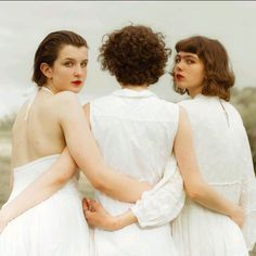 three women in white dresses standing next to each other with their arms around one another