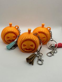 three pumpkin keychains with faces carved into them, one has a tassel and the other has a skull on it