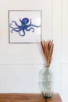 an octopus in a glass vase on a wooden table next to a framed art piece