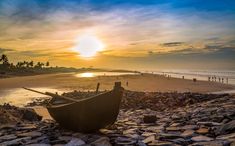 a boat sitting on top of a rocky beach next to the ocean with people in the background