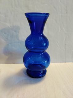 a blue glass vase sitting on top of a wooden table next to a white wall