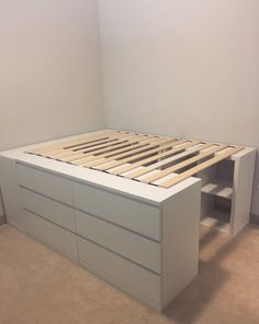 a white bed frame with drawers underneath it in a room that has carpet on the floor