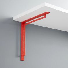 an orange metal shelf is mounted on the wall with a red plastic bracket attached to it