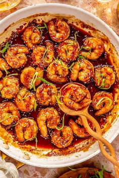 a dish filled with shrimp and sauce on top of a table next to utensils