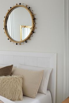 a white bed topped with pillows and a round mirror