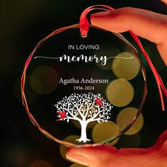 a person holding a glass ornament with a tree on it and the words in loving memory