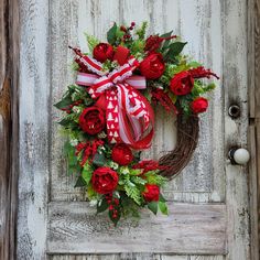 a wreath with red flowers and greenery hangs on a door