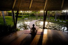 a person sitting on a mat in front of a pond with water lillies at night