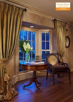 a room with two chairs and a table in front of a window that has curtains on it