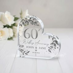 a glass heart shaped object with the number 60 on it and flowers in the background