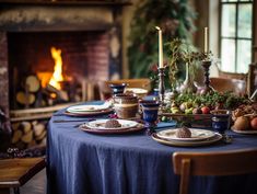 a table set with plates and candles in front of a fire place