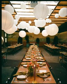 a long table with paper lanterns hanging from it's ceiling and place settings on the tables